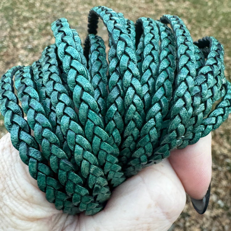 Green braided bracelet cord held in a hand with a blurred natural background