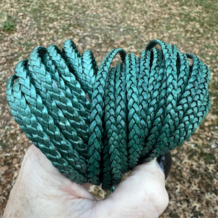 Hand holding a coiled green rope against a textured ground background