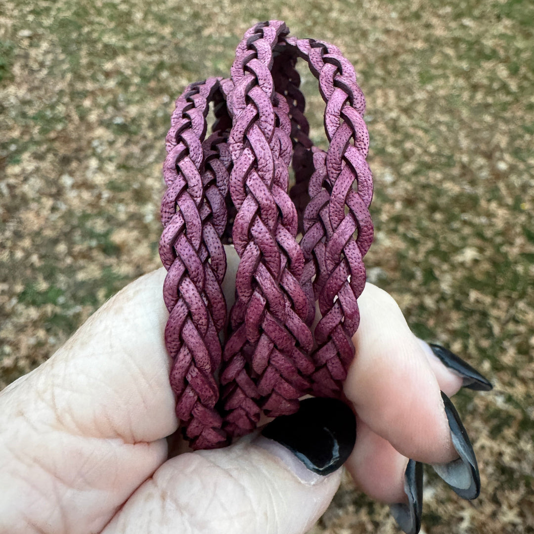 Hand holding a braided purple bracelet against a textured background