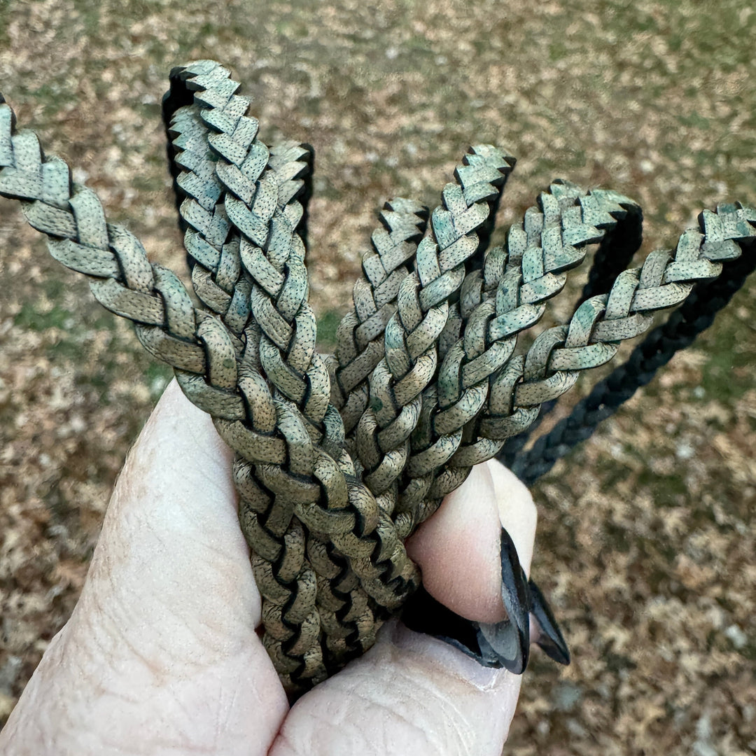 Hand holding a braided olive cord against a blurred natural background