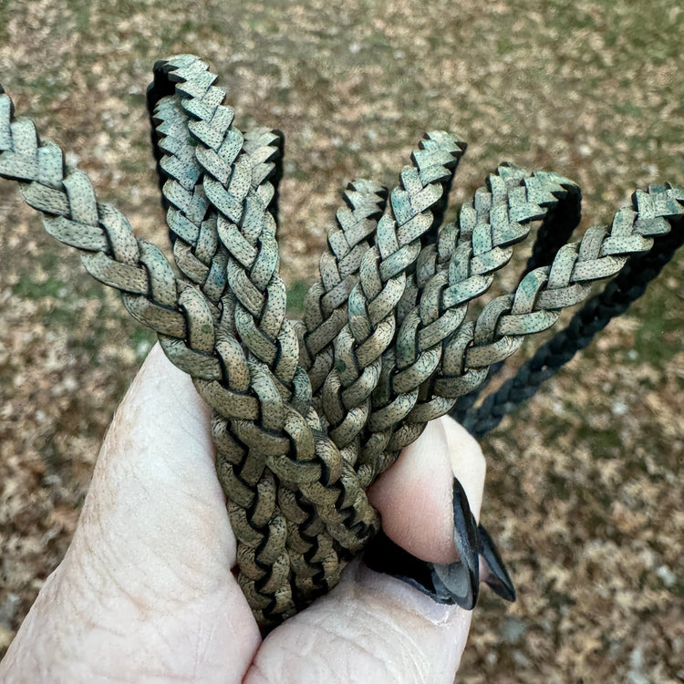 Hand holding a braided olive cord against a blurred natural background